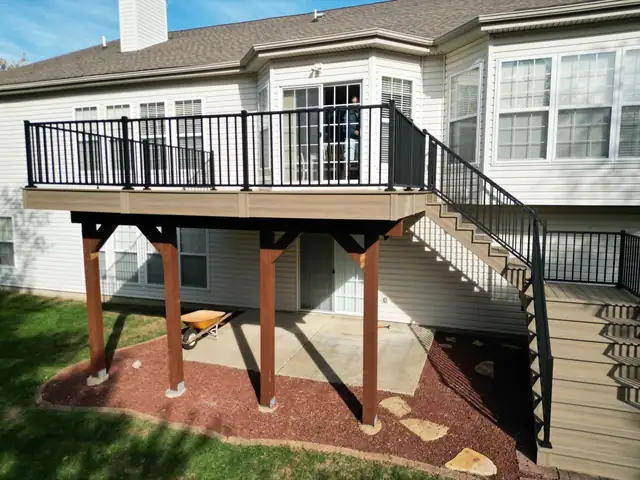 Raised deck with black metal railings, a stairway and wood support posts on a two-story home